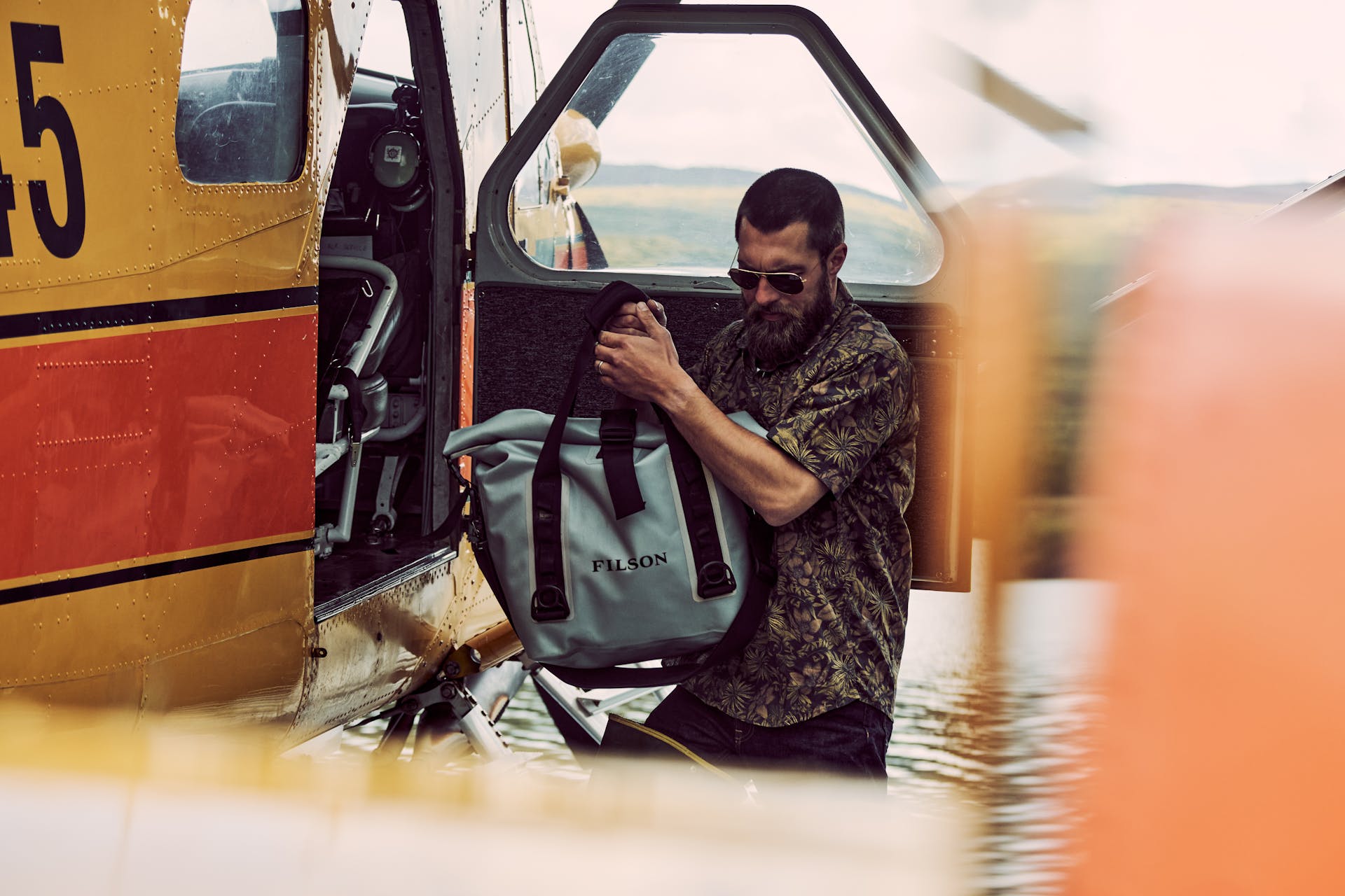 Man carrying a dry bag out of a plane wearing a Filson Washed Short Sleeve Feather Cloth Shirt