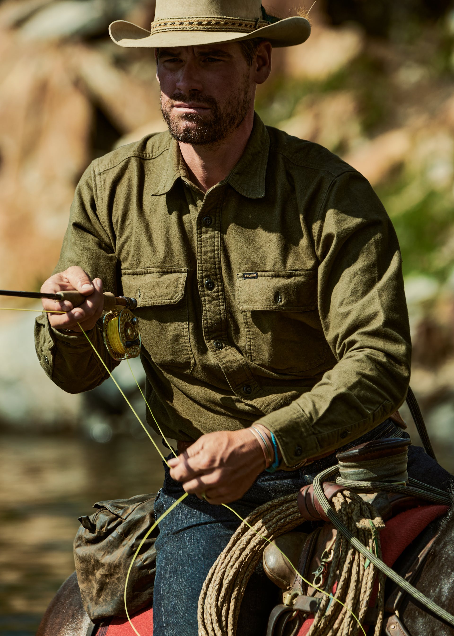 Fisherman riding a horse in the river fly fishing wearing a Filson Field Flannel Shirt