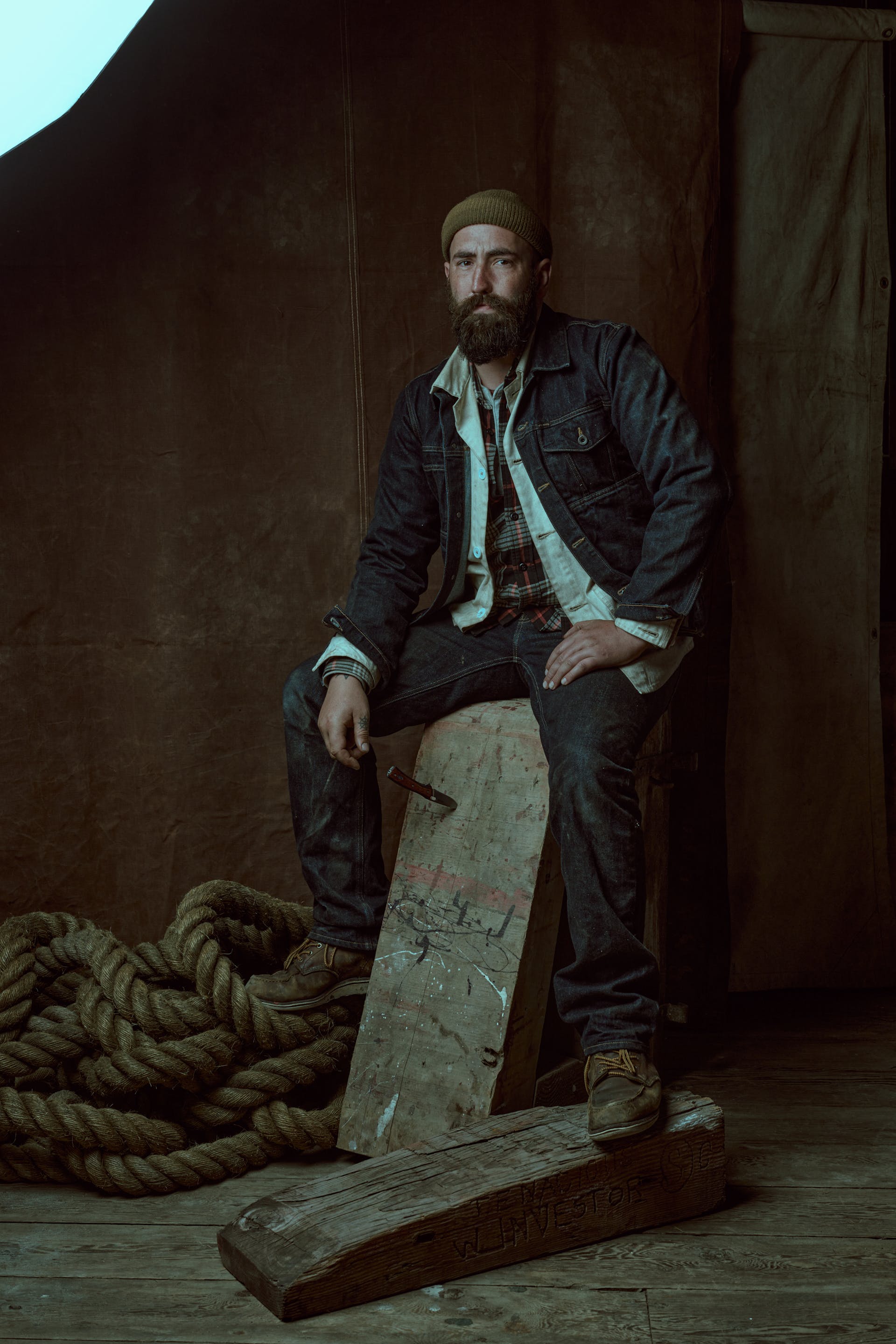Man sitting on an old piece of wooden wearing a Filson Unlined Denim Short Cruiser Jacket