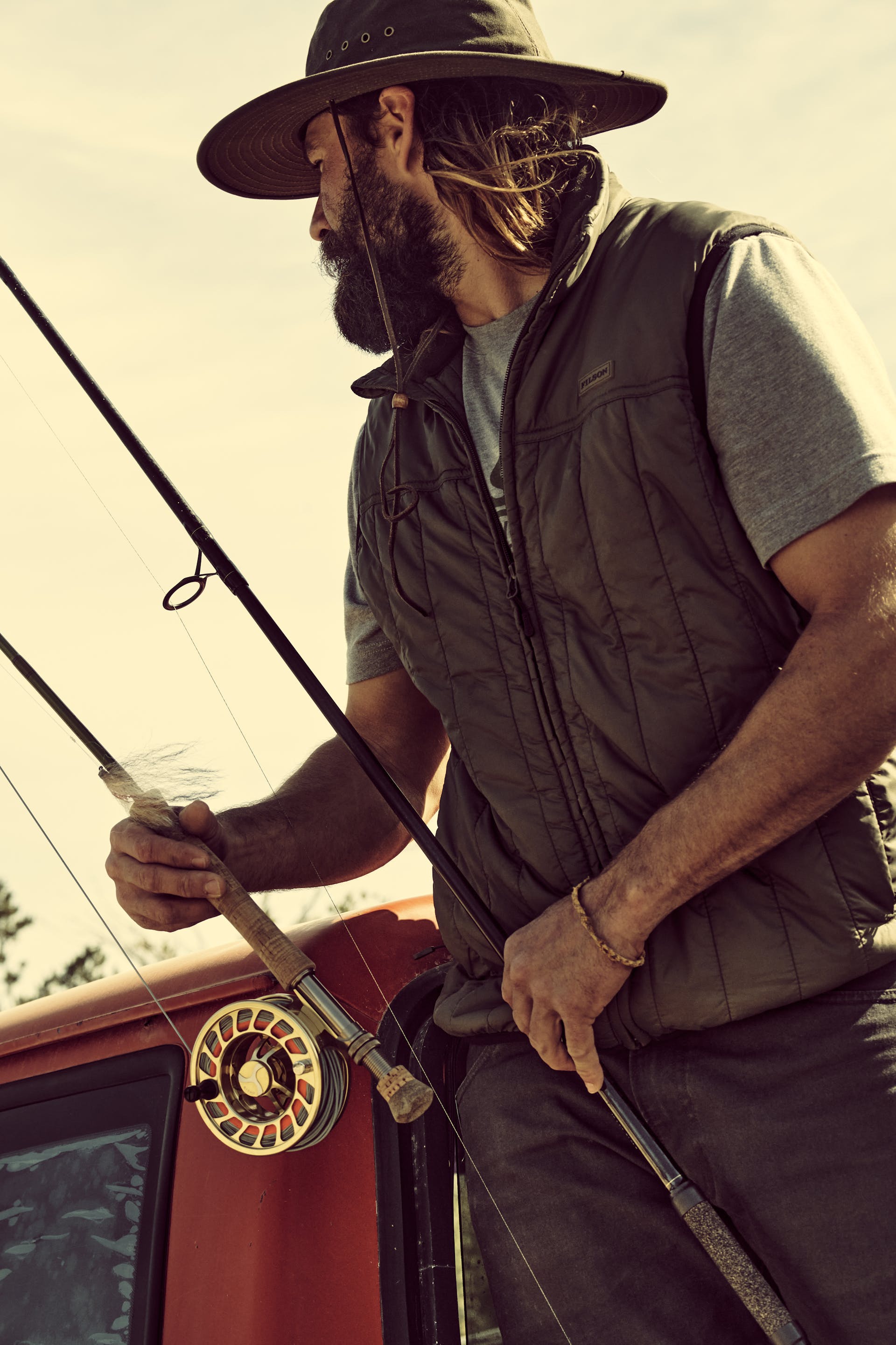 Fisherman holding two rods while wearing a Filson Ultralight Vest in olive gray