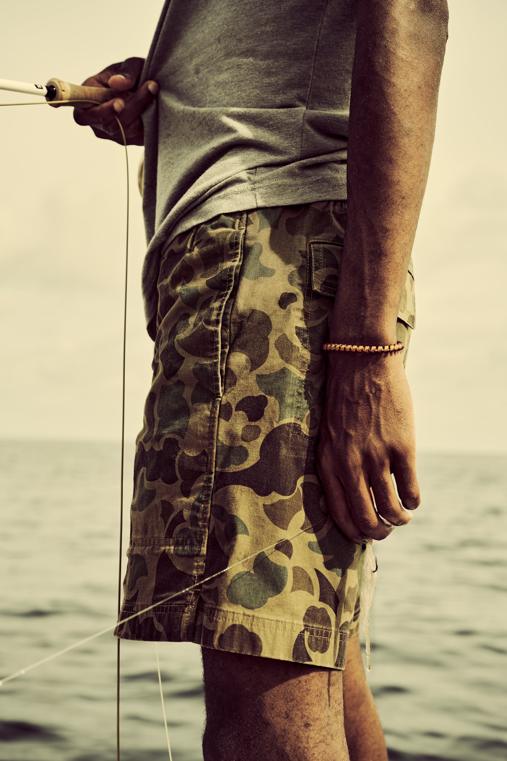Fisherman standing on a boat holding a fishing pole wearing Filson Dry Falls Shorts in surplus shrub camo