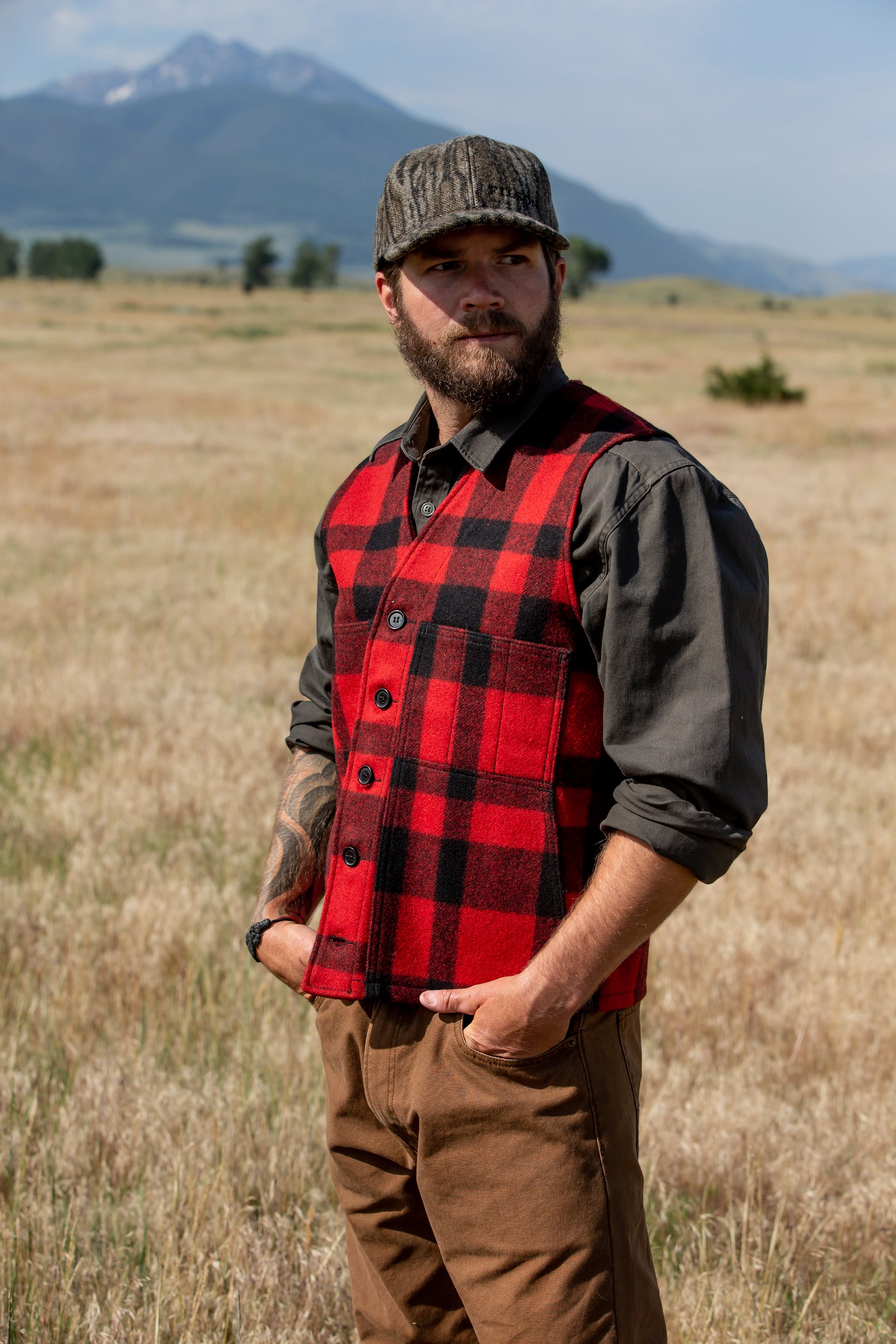 Man wearing Filson Mackinaw Wool Vest in red/black plaid looking outward with his hands in his pant pockets
