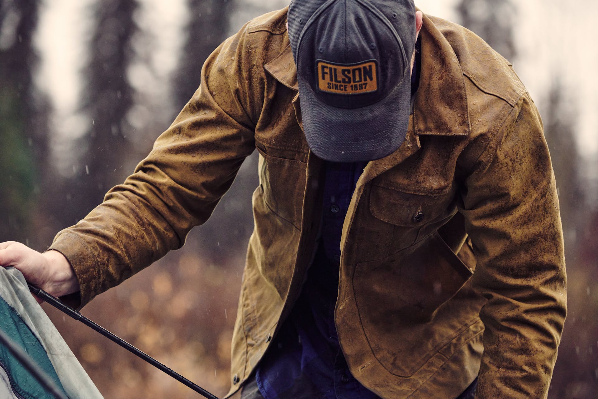 Man setting up a tent in rainy Alaska while wearing a Filson Tin Cloth Short Lined Cruiser in dark tan