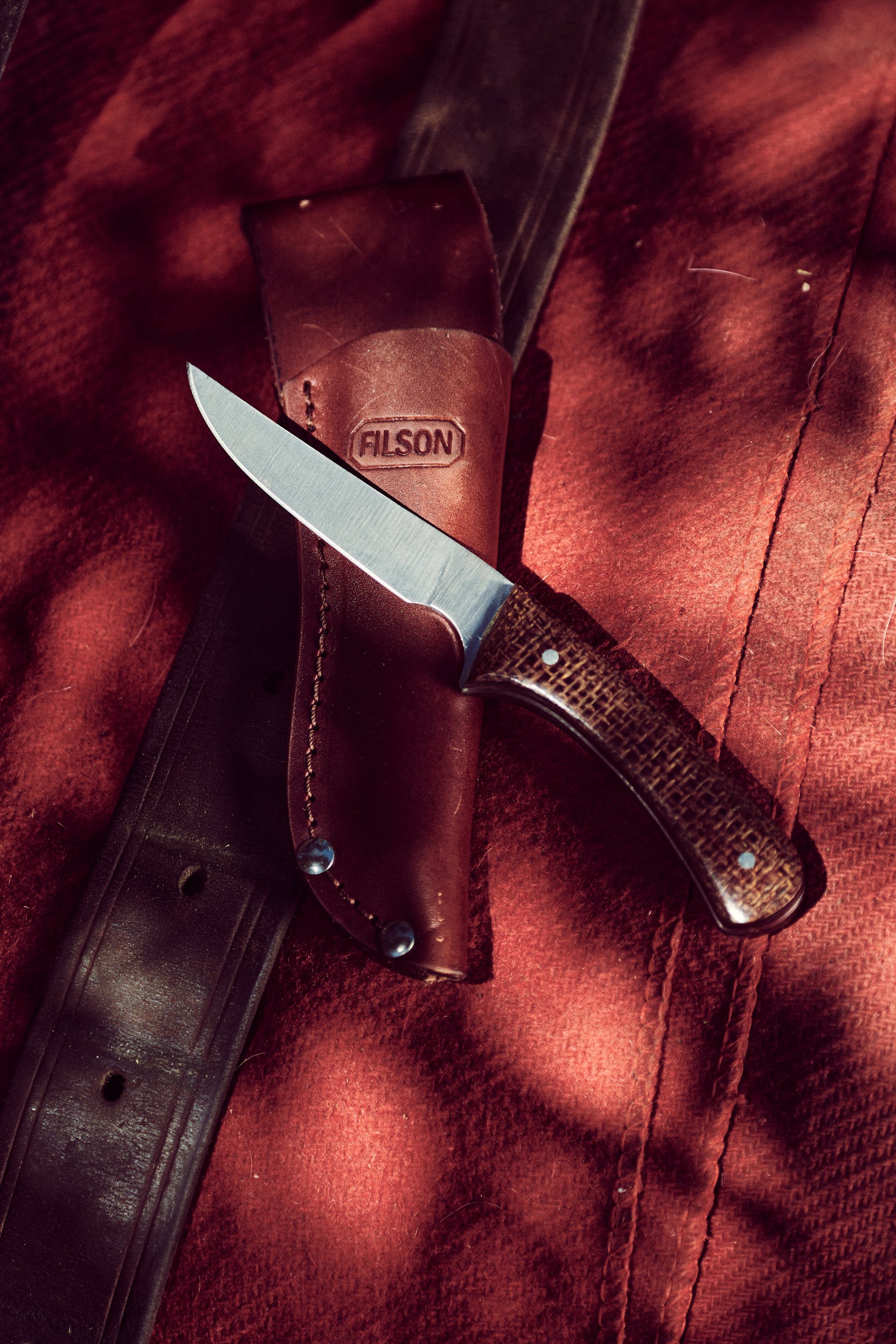 Filson Bird & Trout Knife resting on its sheath on red fabric