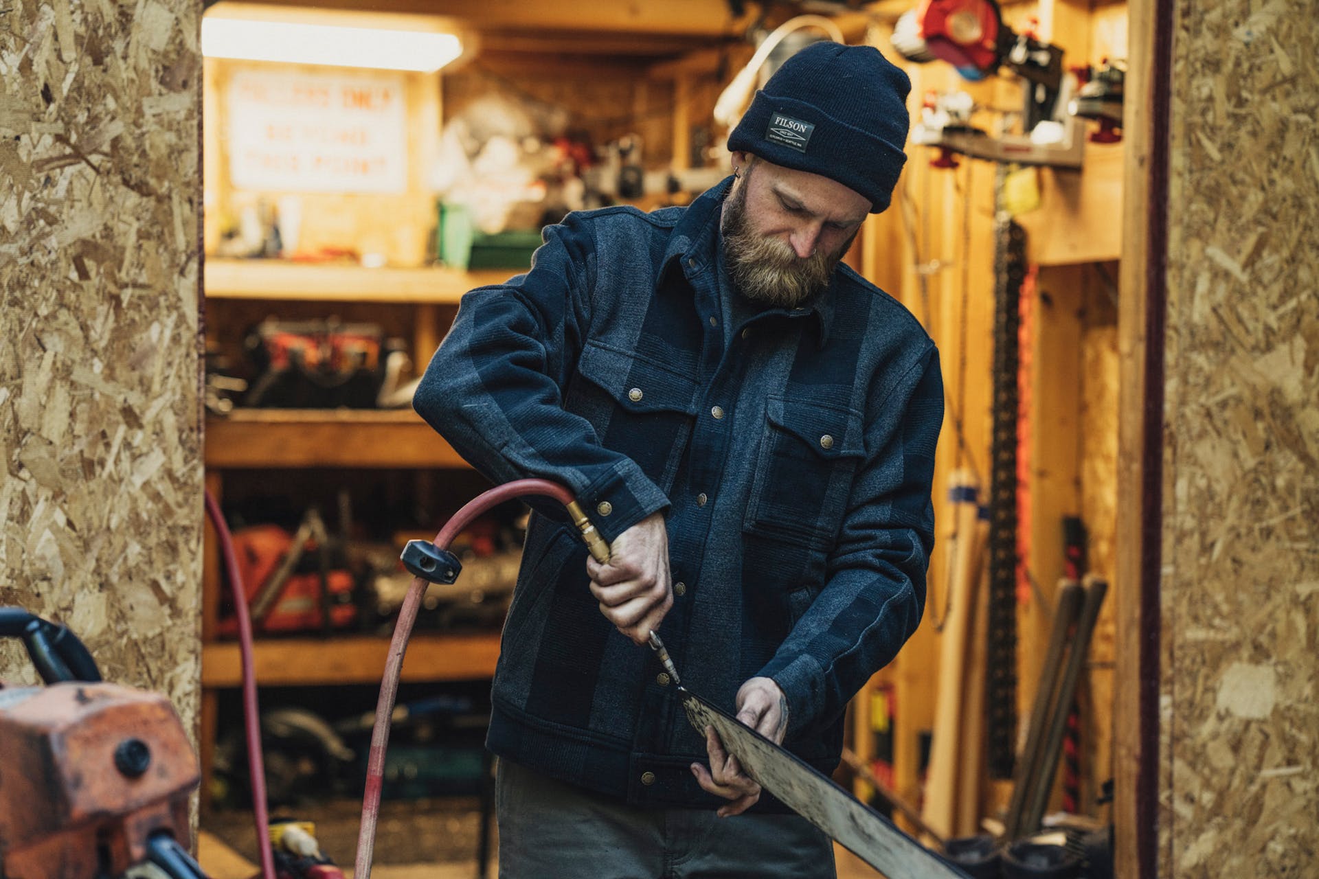 Man cleaning a chainsaw blade with an air compressor wearing a Filson Ballard Watch Cap in black