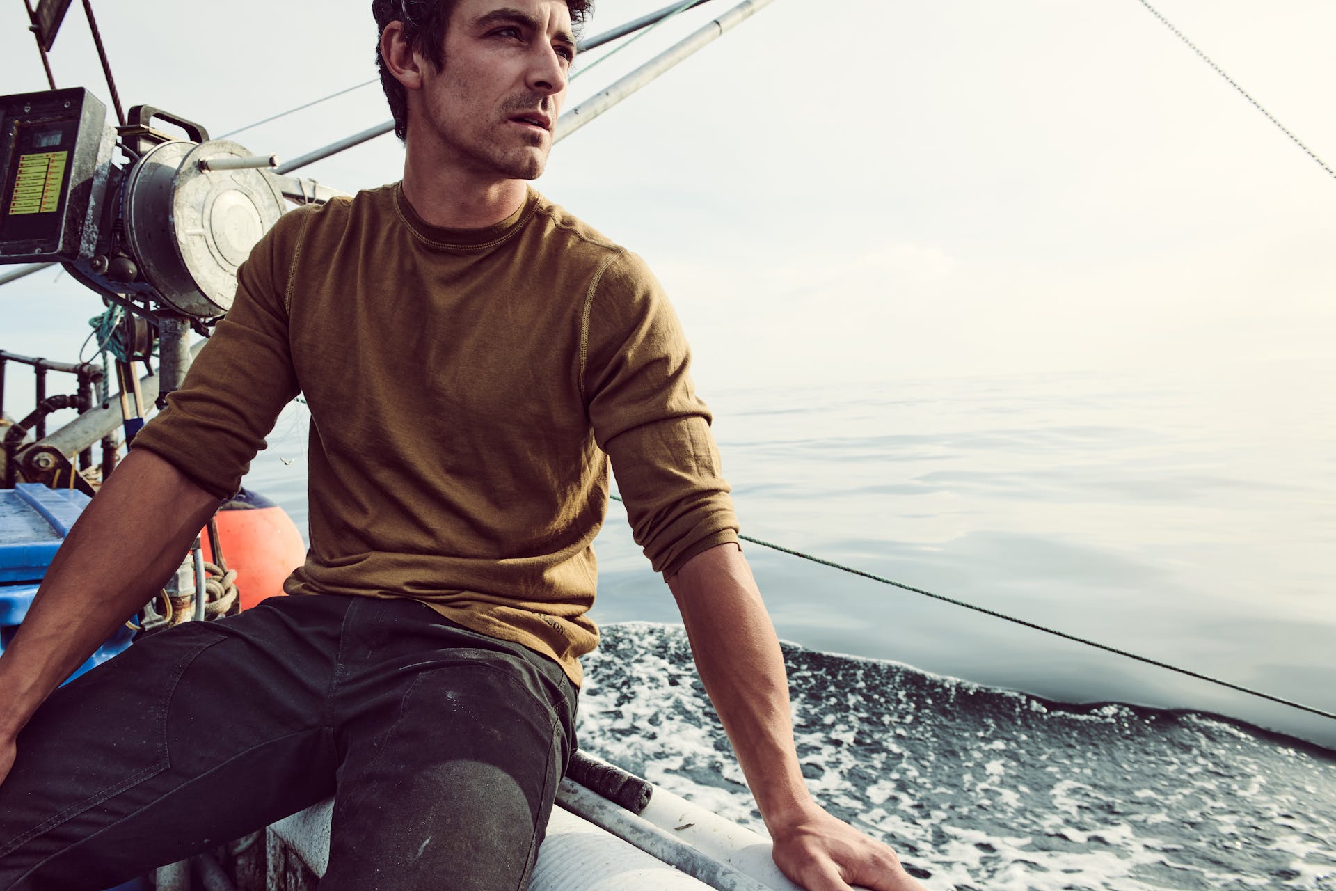 Fisherman sitting on the edge of a boat wearing a Filson 280G Merino Long Sleeve Crew shirt