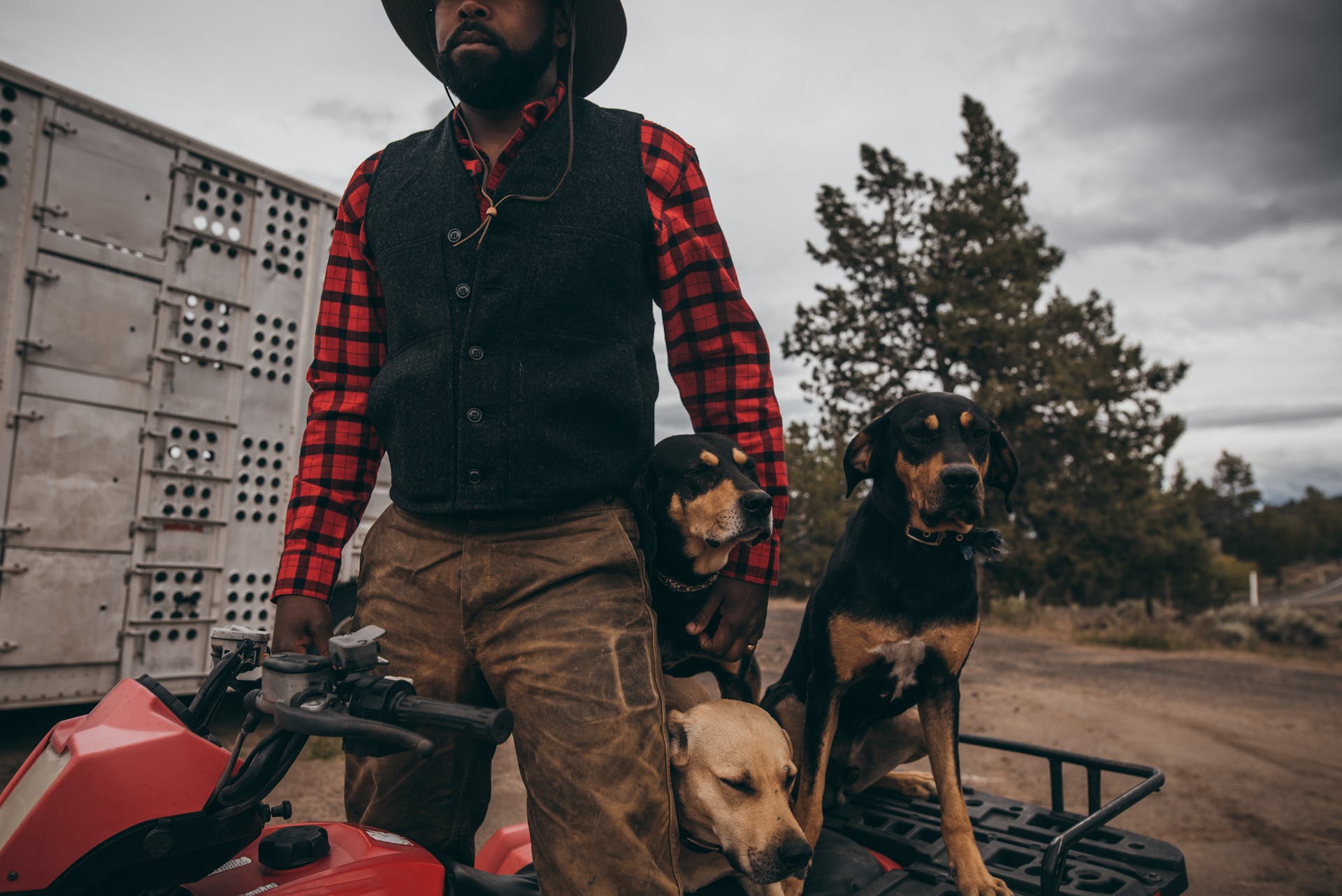 Man wearing Filson Mackinaw Wool Vest in charcoal standing on an ATV with three dogs