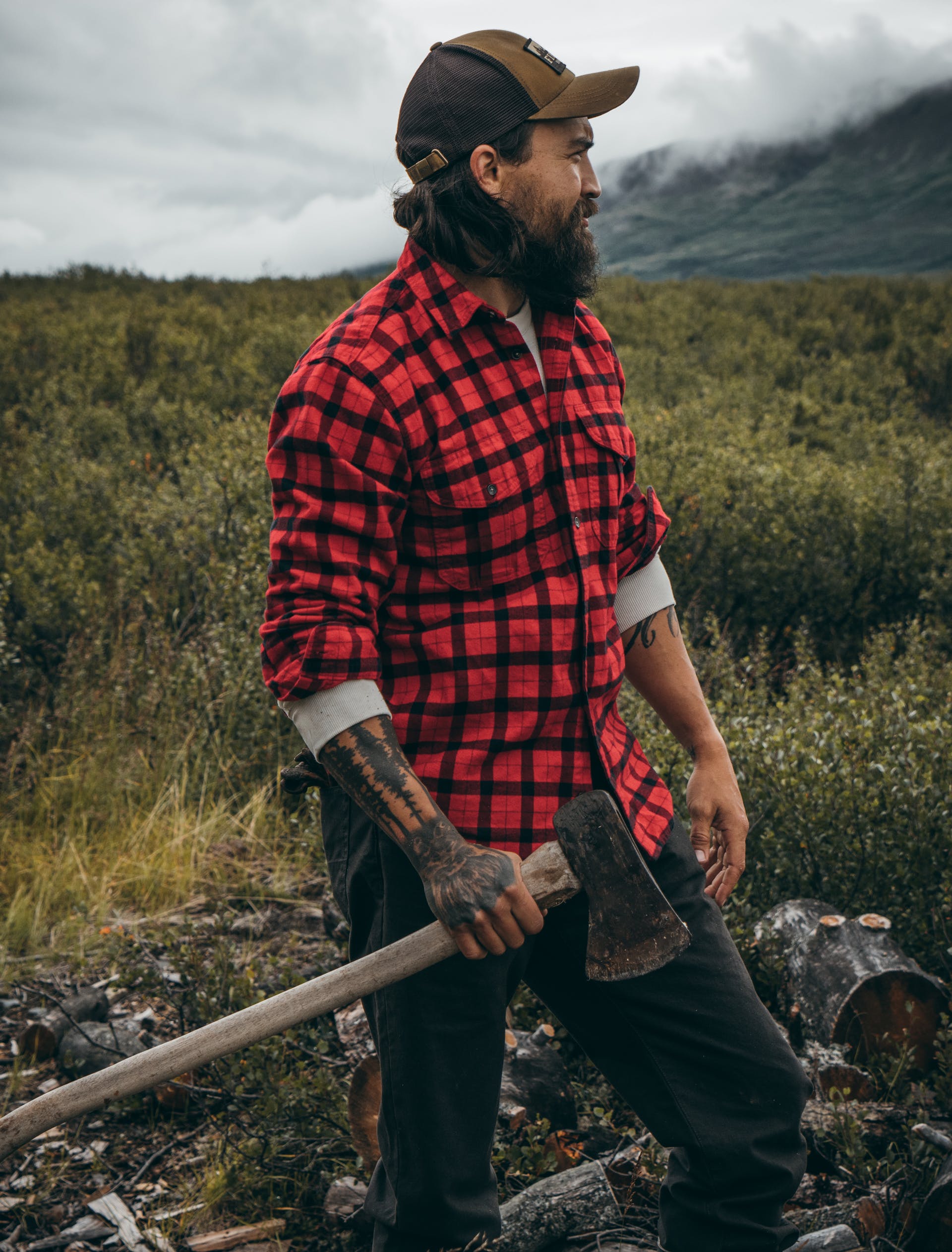 Man standing in a field with an axe chopping wood in a Filson Alaskan Guide Shirt