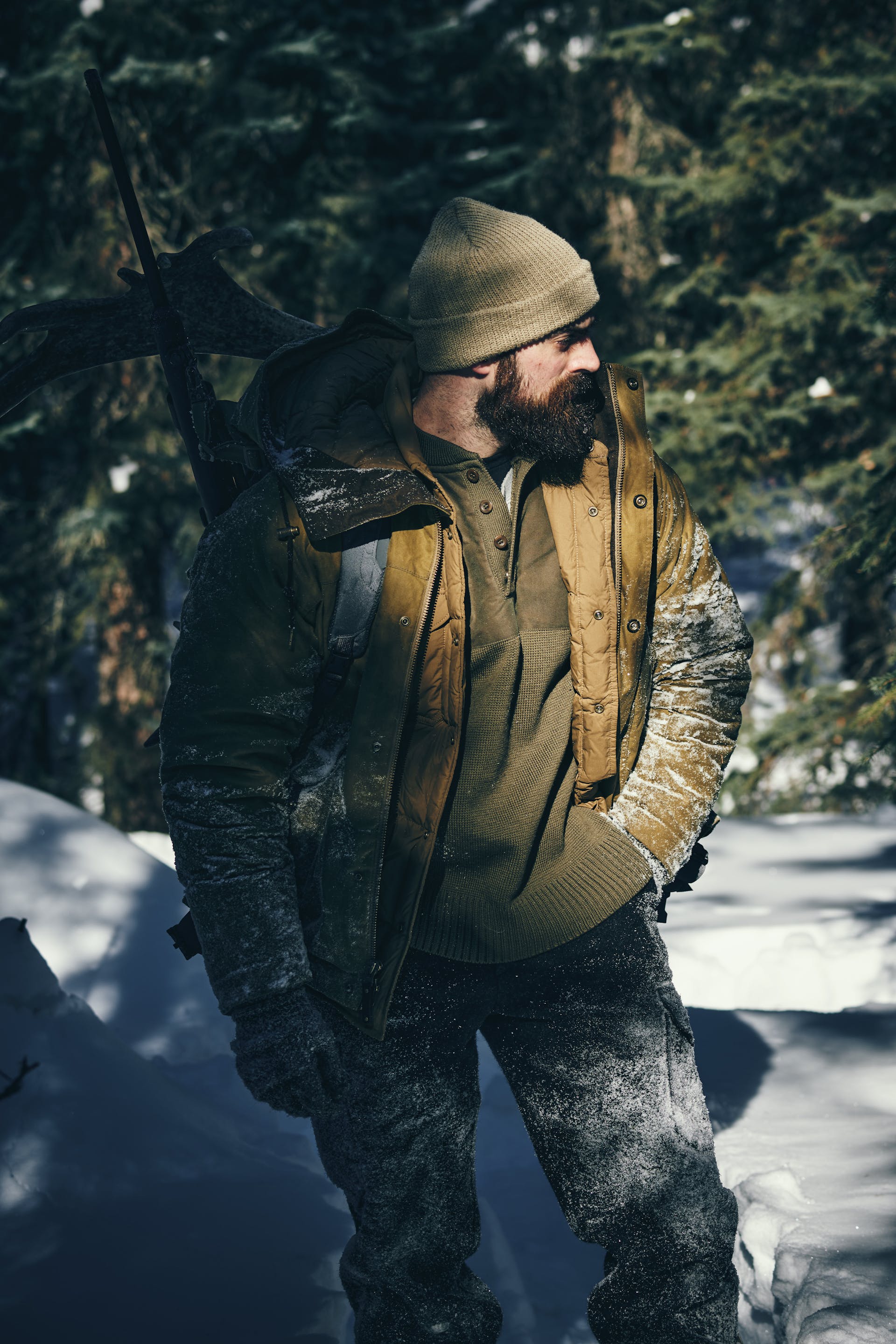 Man wearing Filson Henley Guide Sweater in peat green walking through snow and looking around