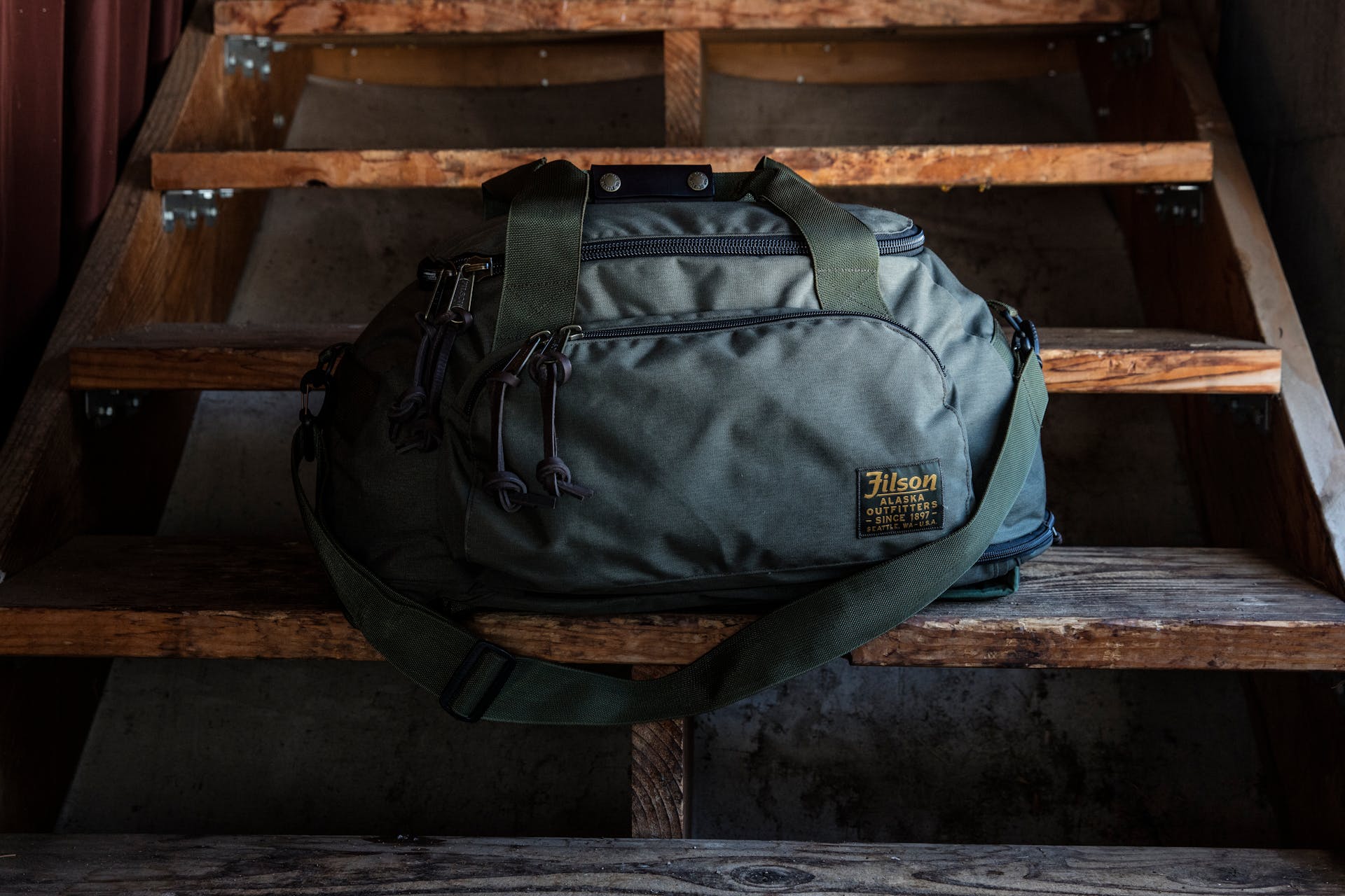Filson Duffle Pack in otter green resting on wooden staircase