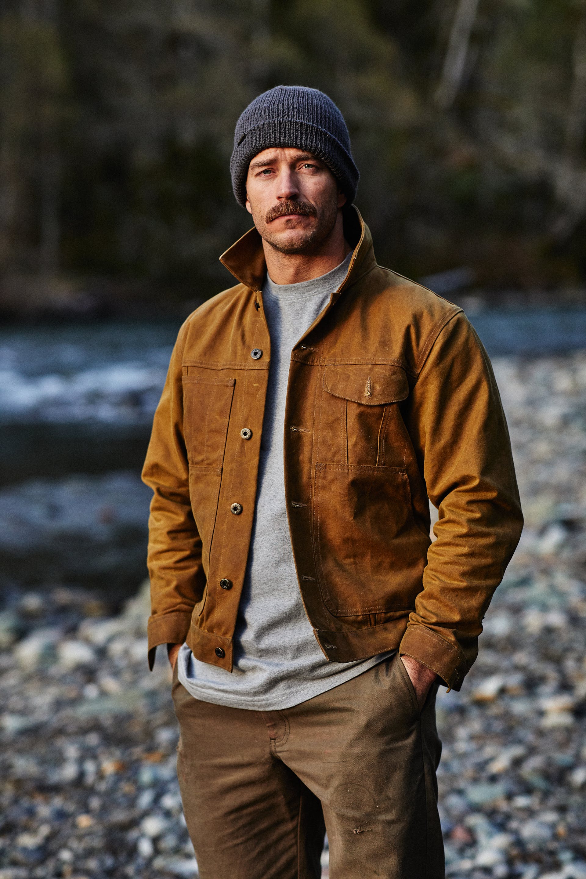 Man standing on the bank of a river wearing a Filson Tin Cloth Short Lined Cruiser Jacket in dark tan.