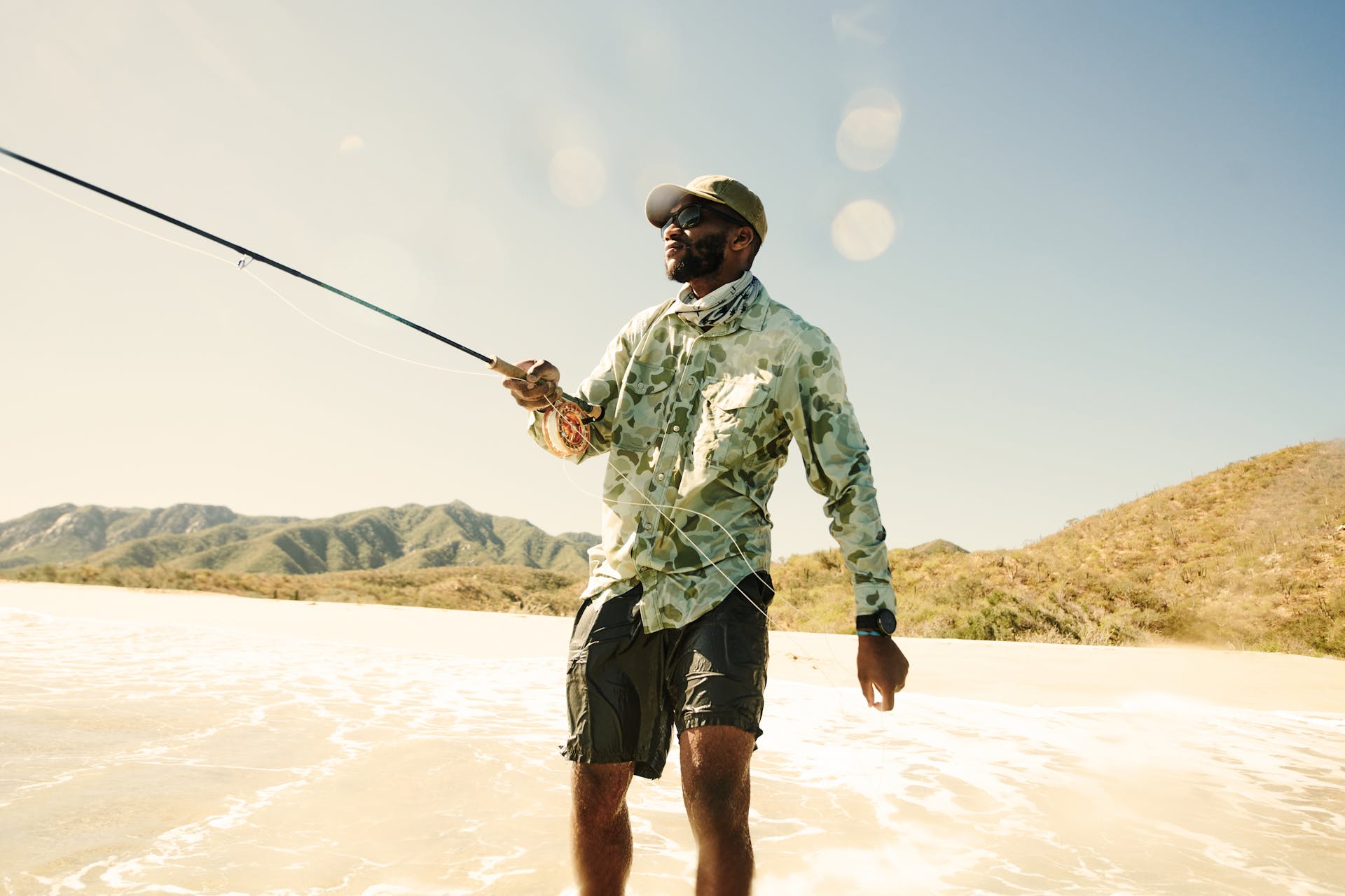 Man wearing Filson Twin Lakes Sport Shirt in sage shrub camo standing in water and holding up a fishing rod