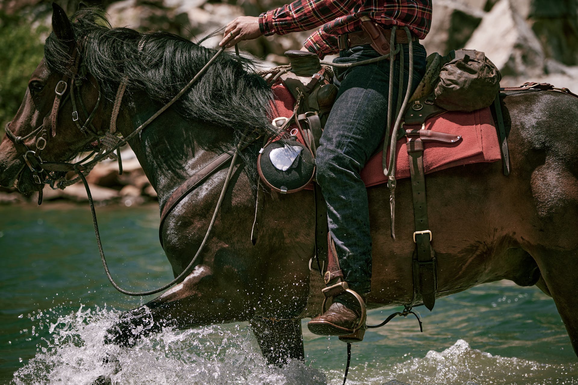 Man riding a horse through water with a Filson Bird & Trout knife in a sheath on his saddle